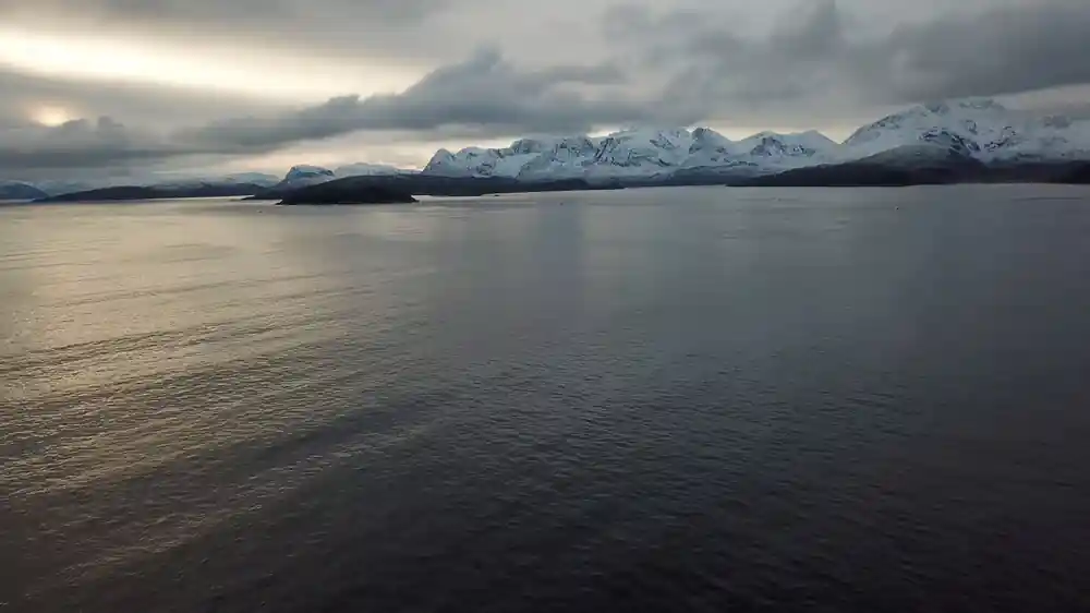 A dark fjord with cloud sitting on the snow ridges beyond