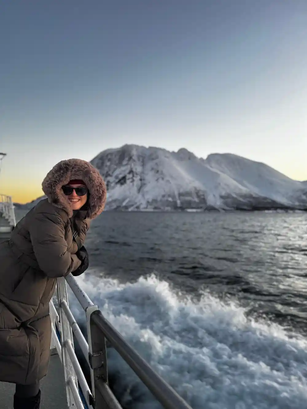 A passenger in a fur-trimmed hood at the rail with mountains behind