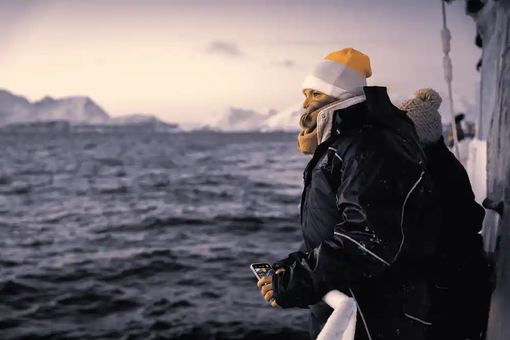 A passenger in a yellow hat at the rail watching the water