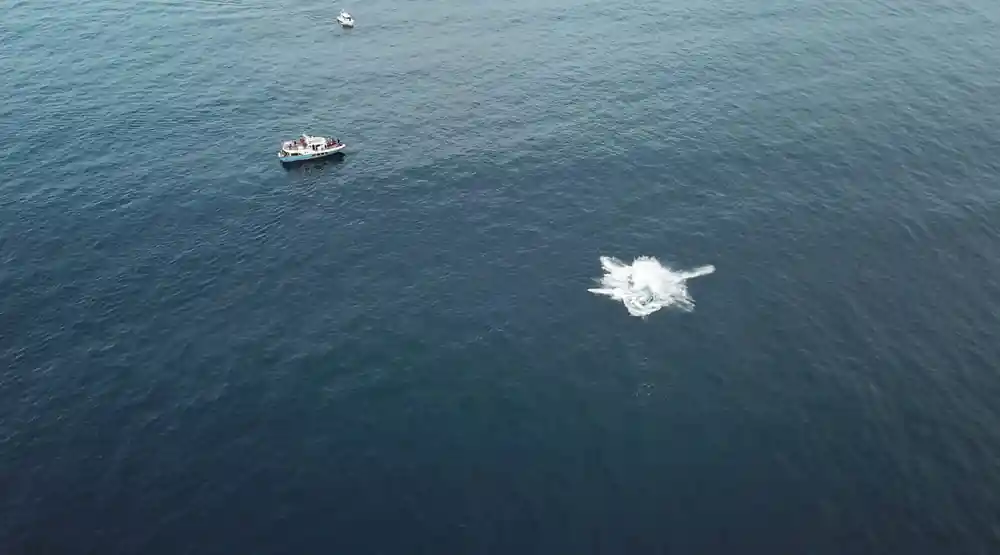 A small boat and a whale blow together on an empty grey sea
